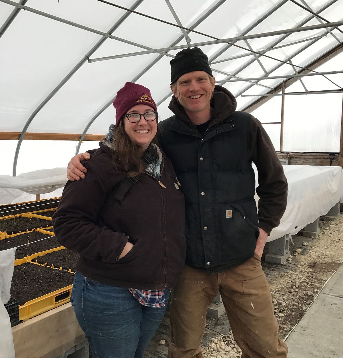 woman and man side hug in a hoop house in winter clothes