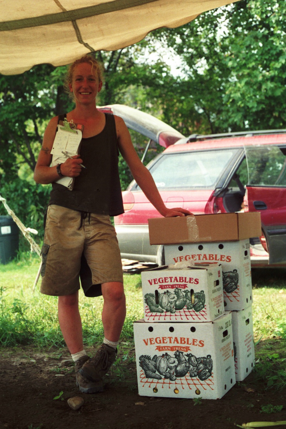 woman with clipboard stand next to boxes full of produce