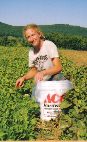 women kneels in field holding pepper